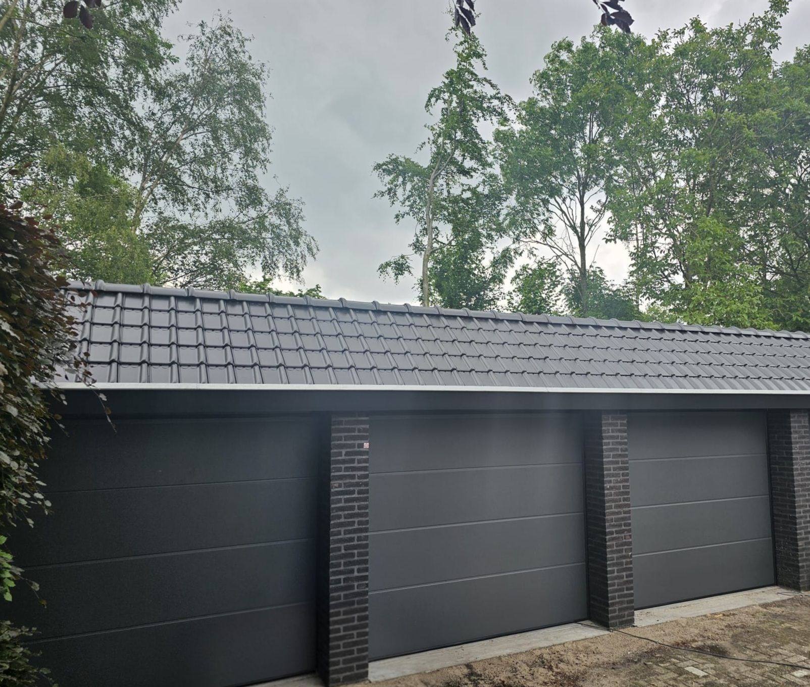 Rij van drie antracietkleurige garagedeuren onder een pannendak