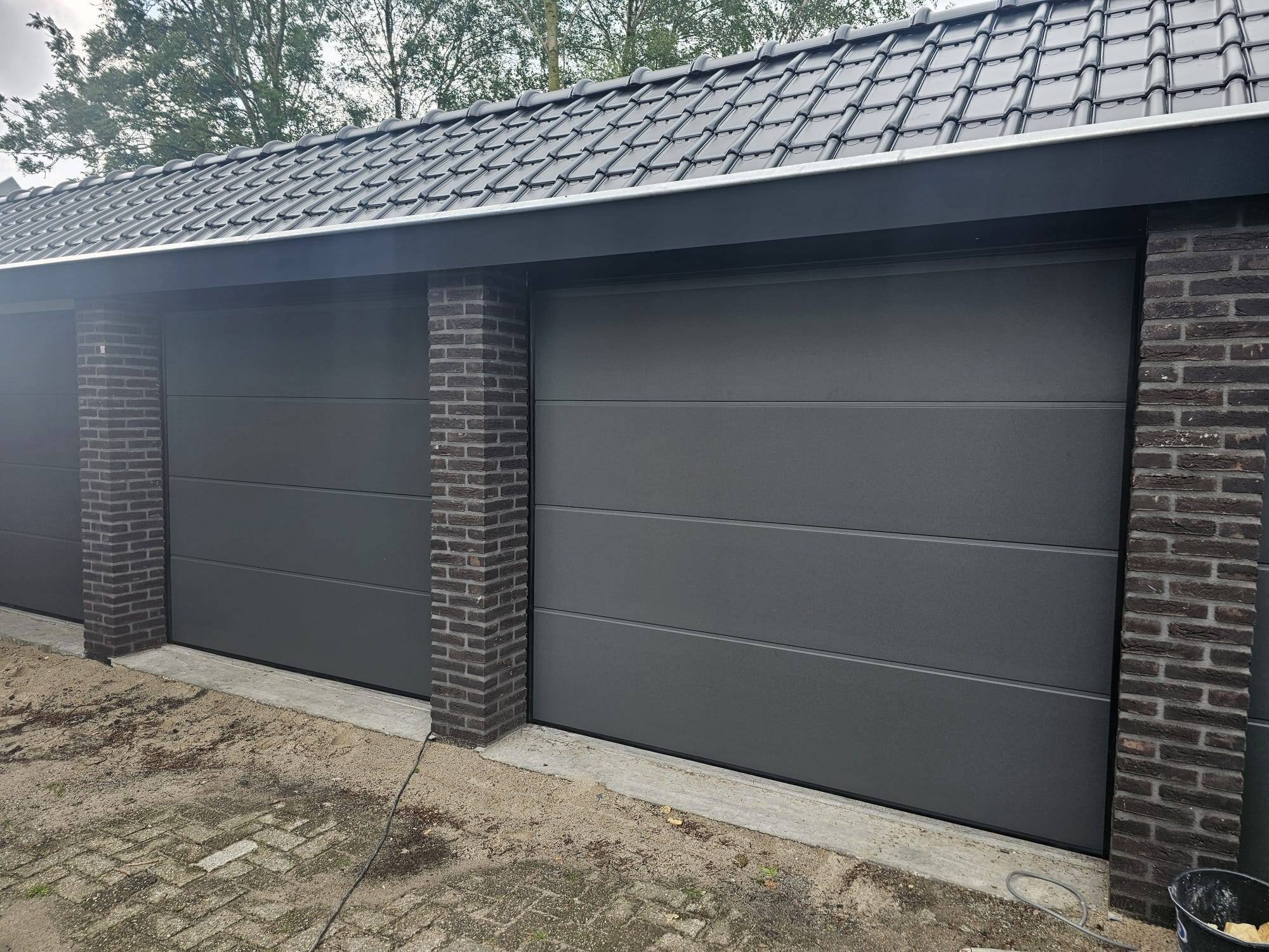 Twee antracietkleurige sectionaal garagedeuren tussen gemetselde penanten