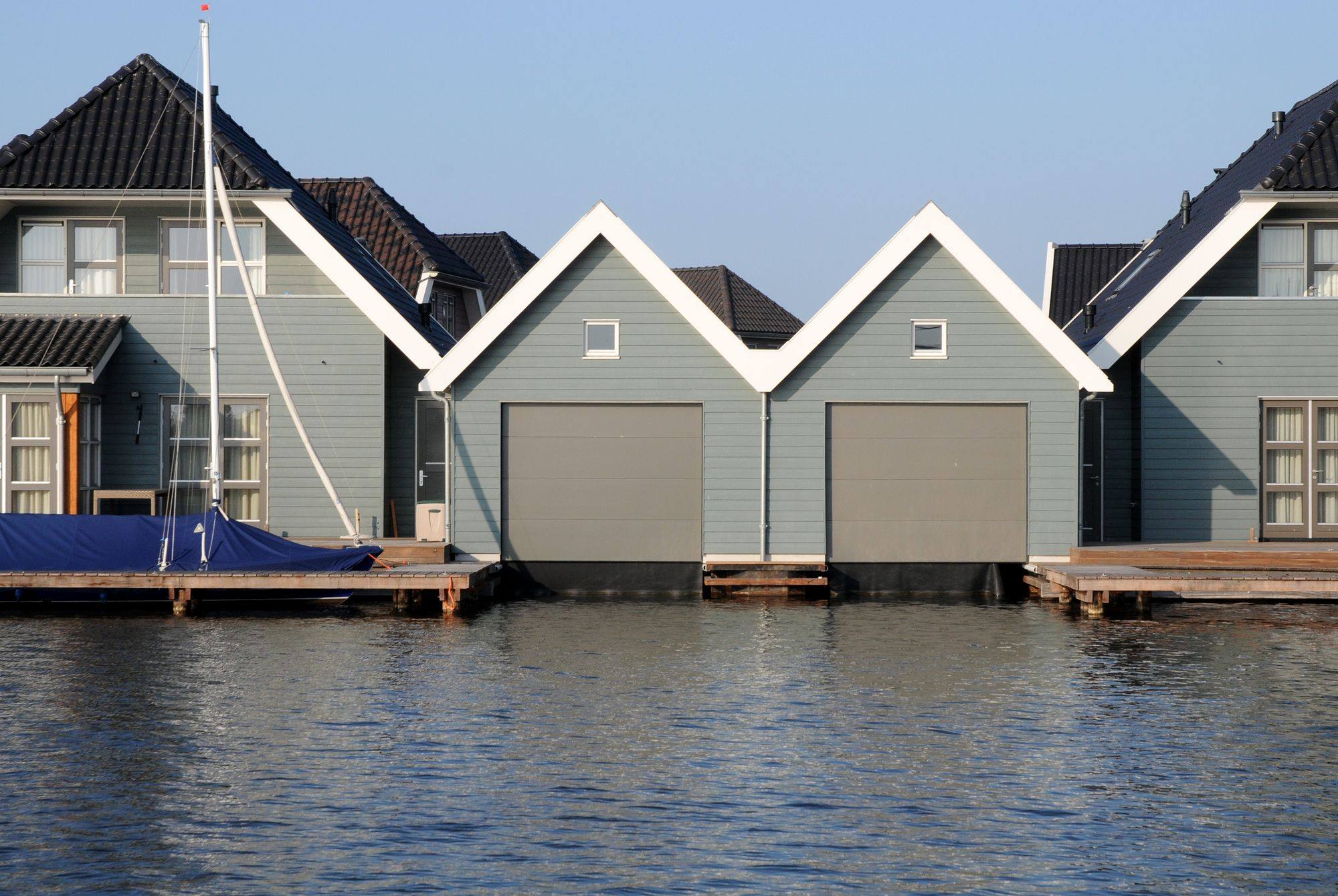 Grijze sectionaaldeuren in drie botenhuizen aan het water