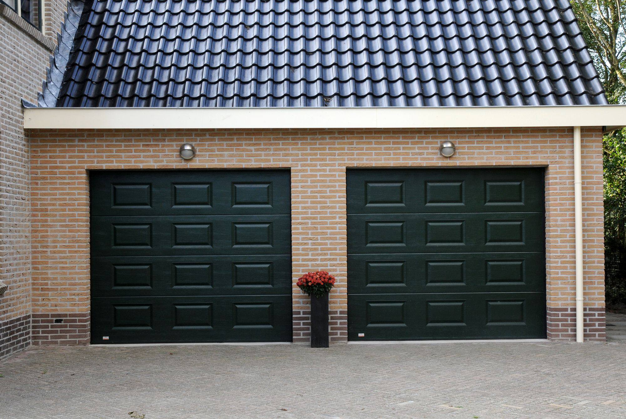 Twee donkergroene garagedeuren met cassettemotief in een gele bakstenen gevel