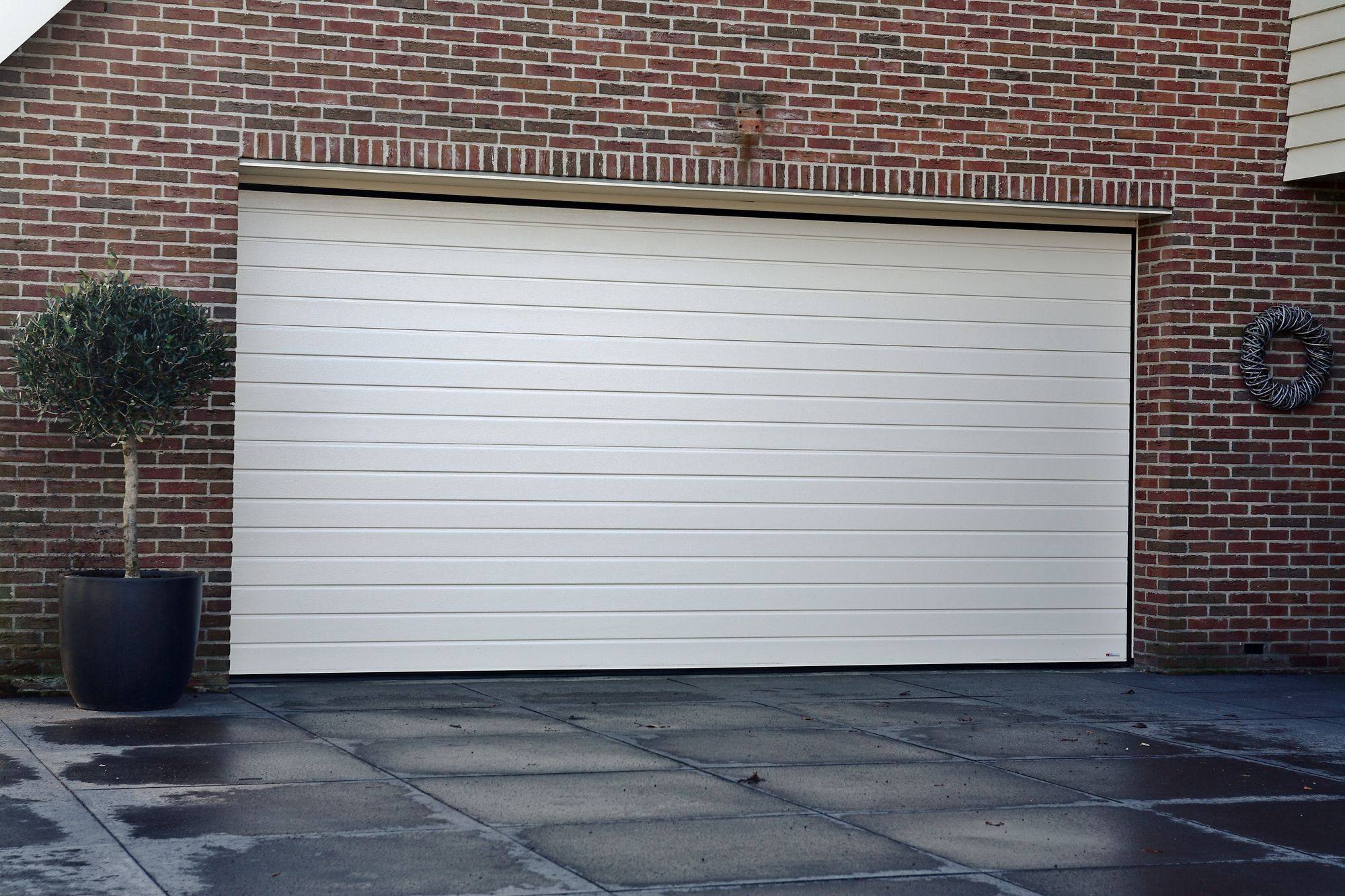 Witte sectionaal garagedeur met fijne lijnen in een rode bakstenen gevel