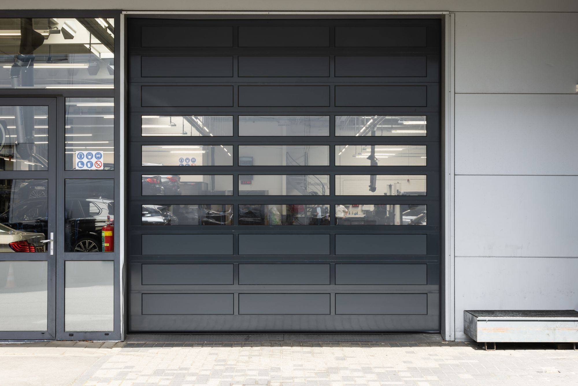 Zwarte industriedeur met glaspanelen naast een glazen entree