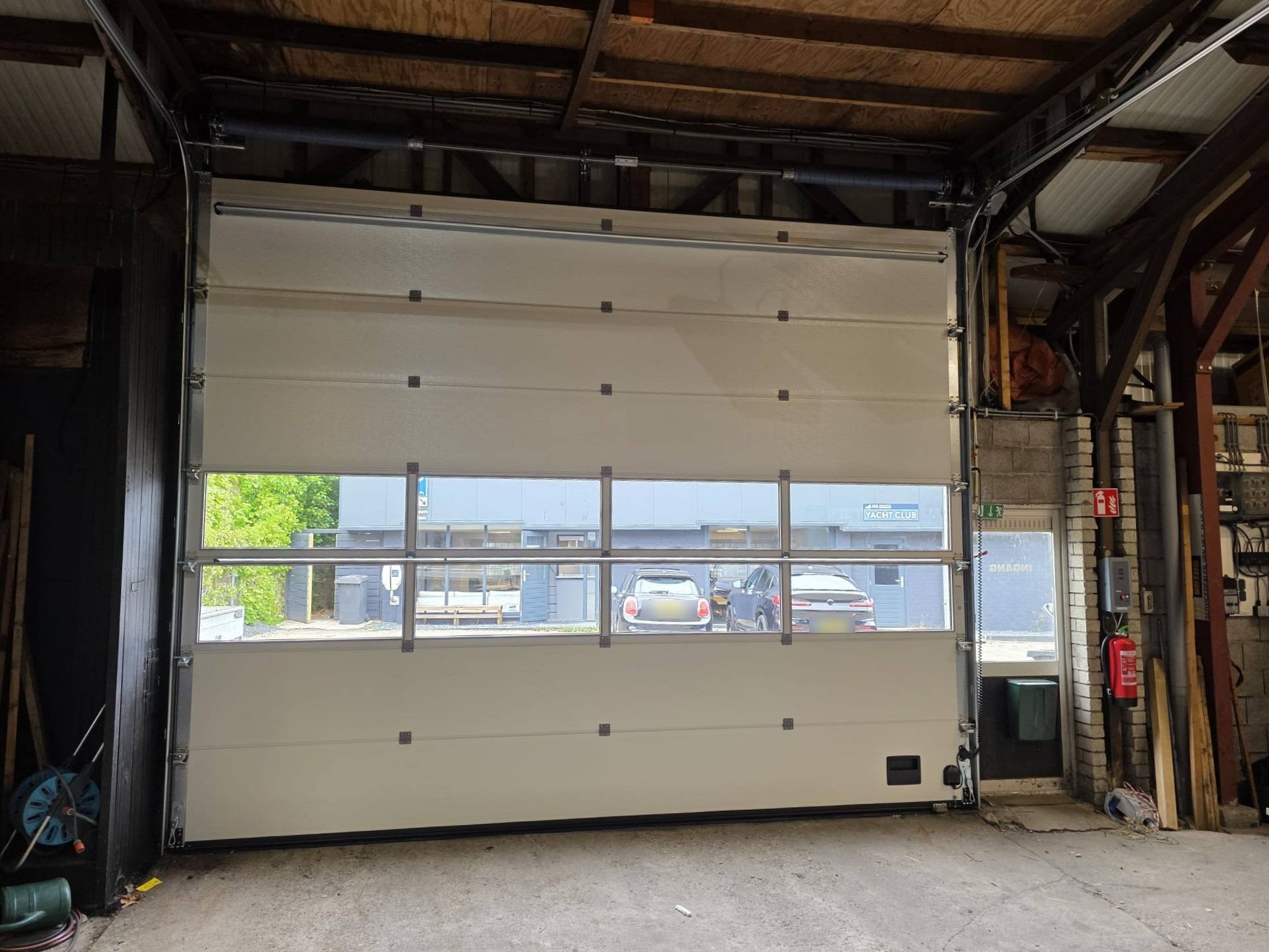 Binnenzijde van een witte industriedeur met glassectie, veren en geleiding zichtbaar