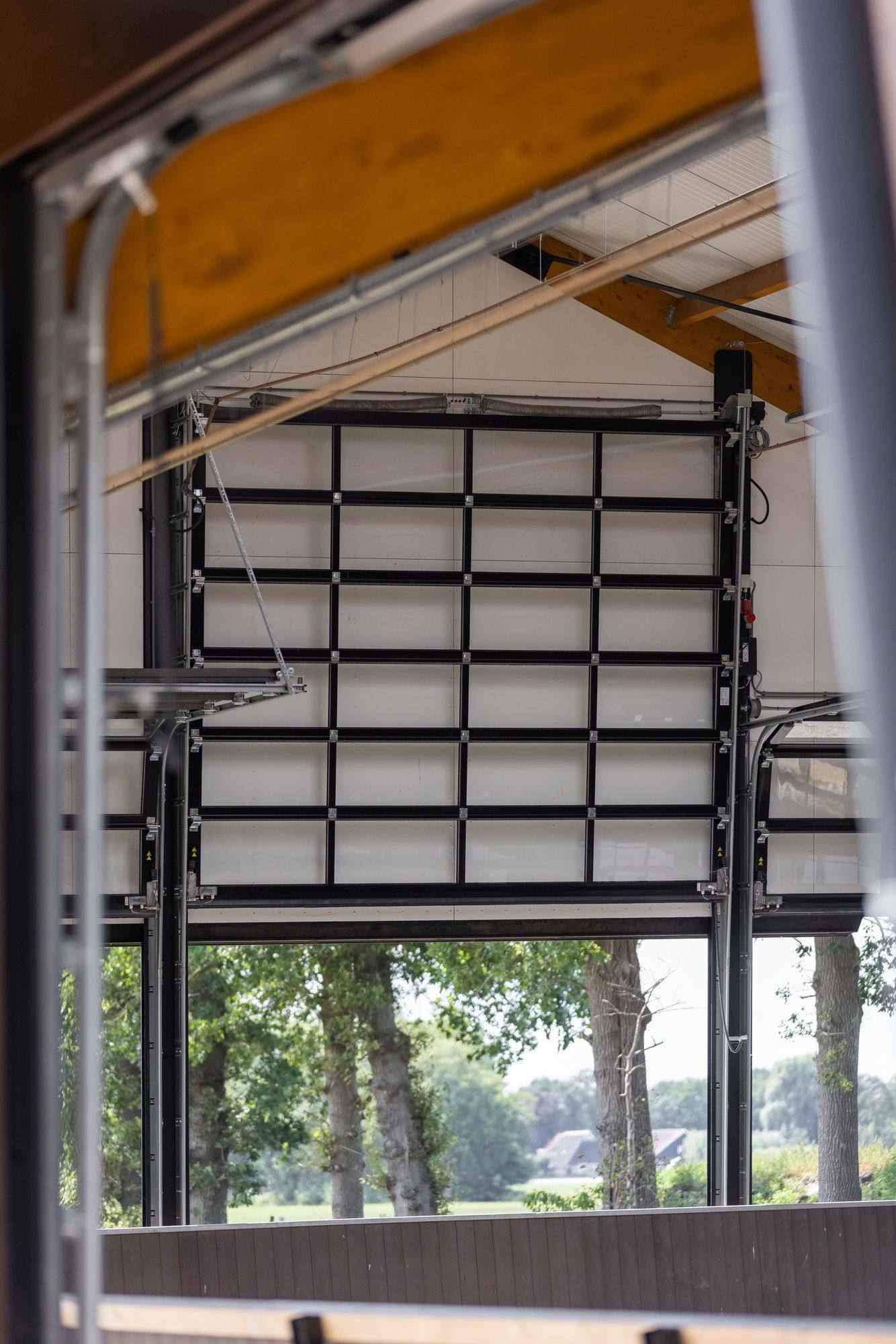 Glazen sectionaaldeur half geopend onder een houten dakconstructie, met rails en ophanging