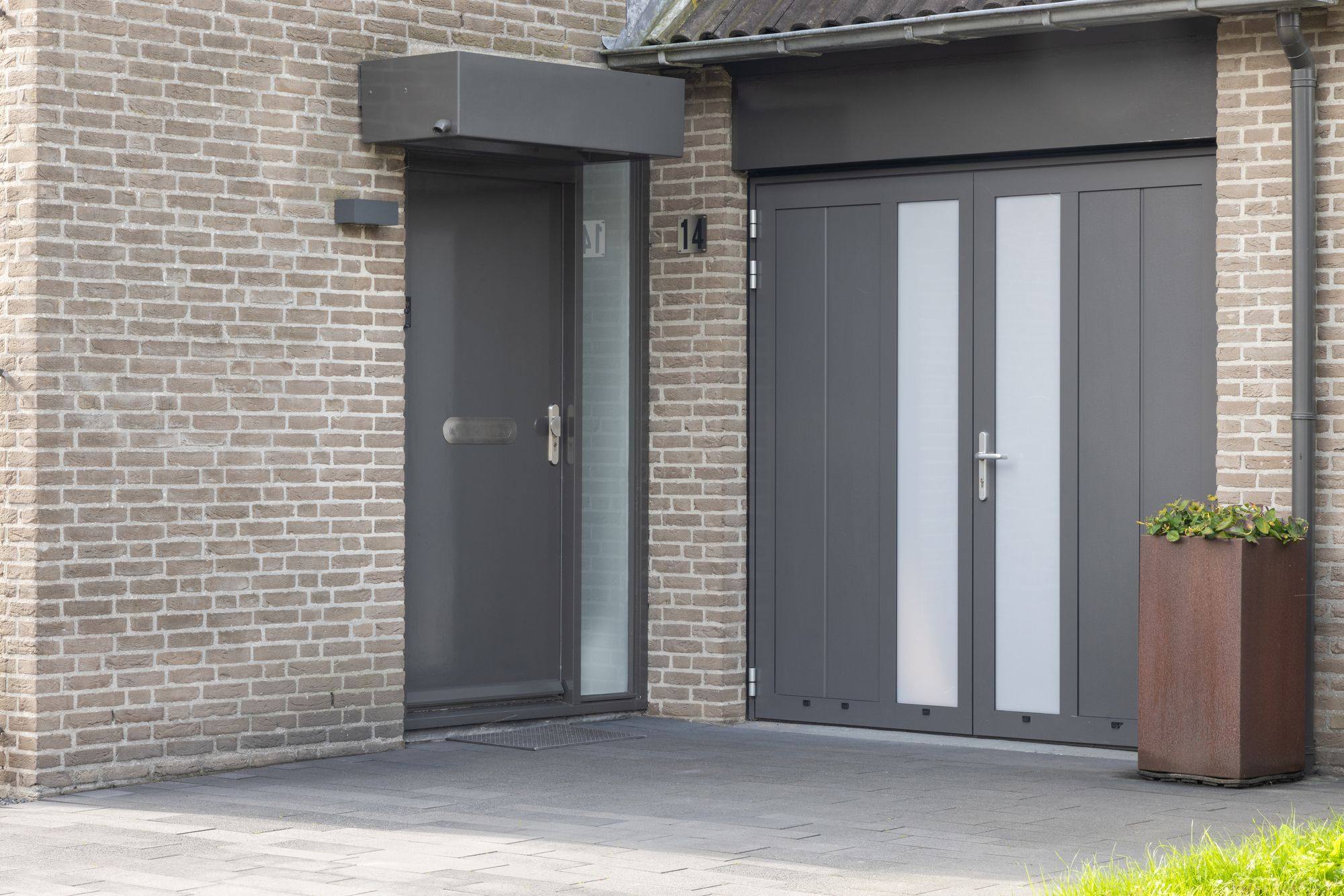 Grijze openslaande garagedeur met matglazen stroken naast een voordeur