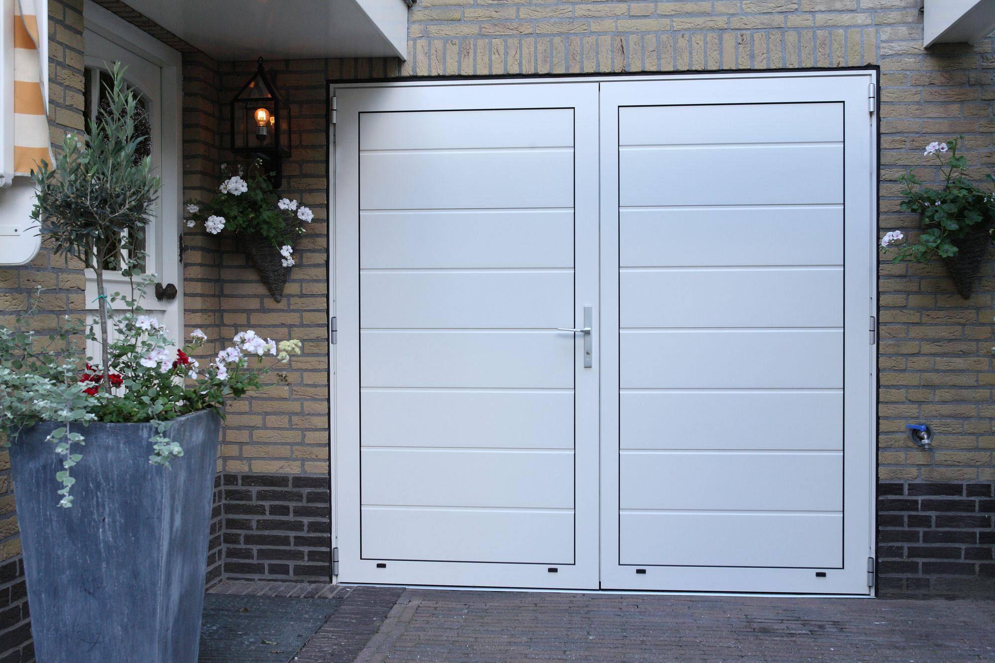 Witte openslaande garagedeur met bloembakken ernaast